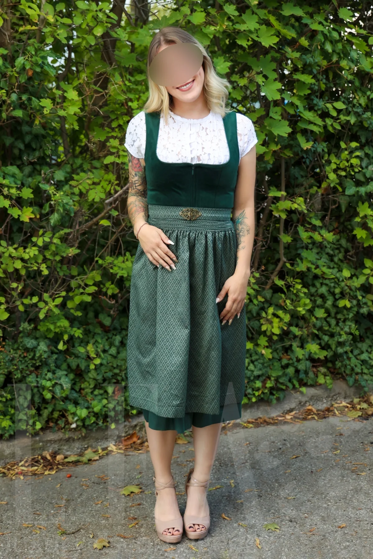 Escort Julia aus München im grünen Dirndl vor der Hecke