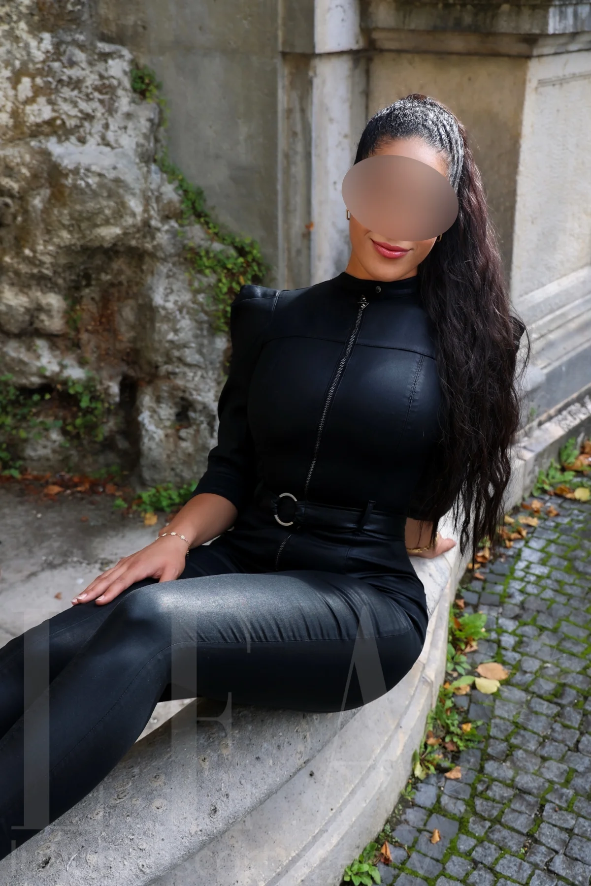 Escort Begleitung Stella aus München im Lederoverall auf der Treppenmauer