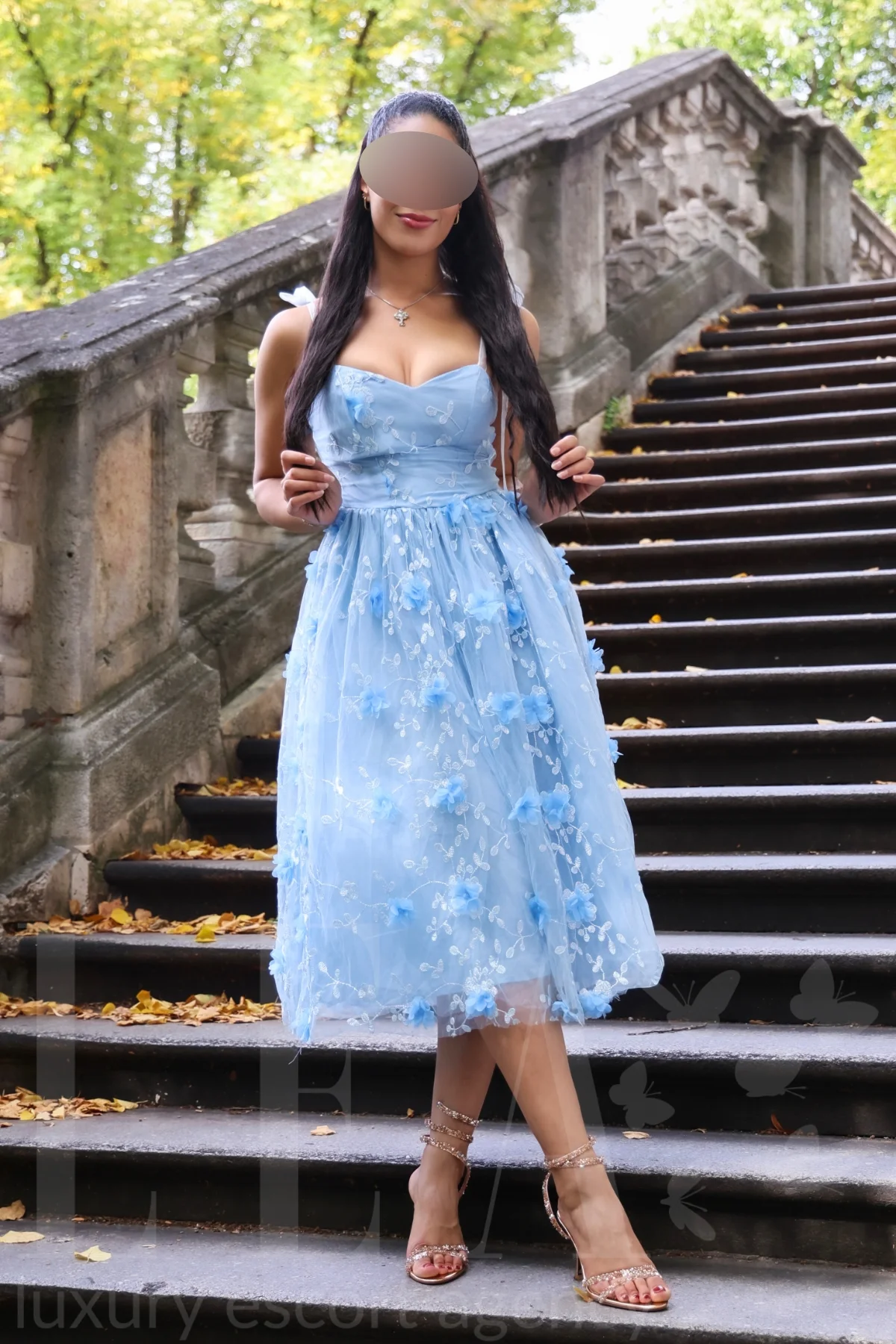 Escort Model Stella in München im hellblauen Blütenkleid auf der Parktreppe