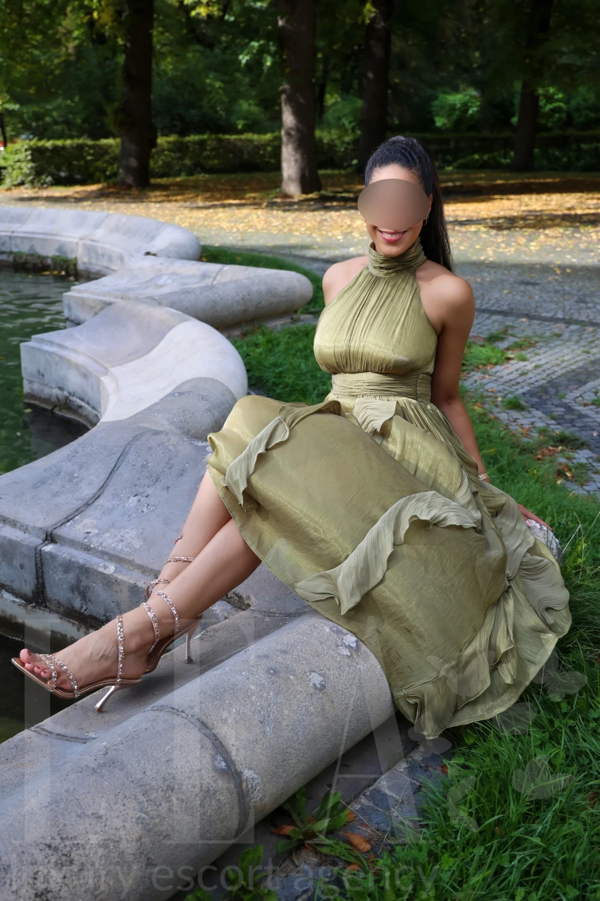 Escort Stella in München im olivgrünen Kleid am Brunnen